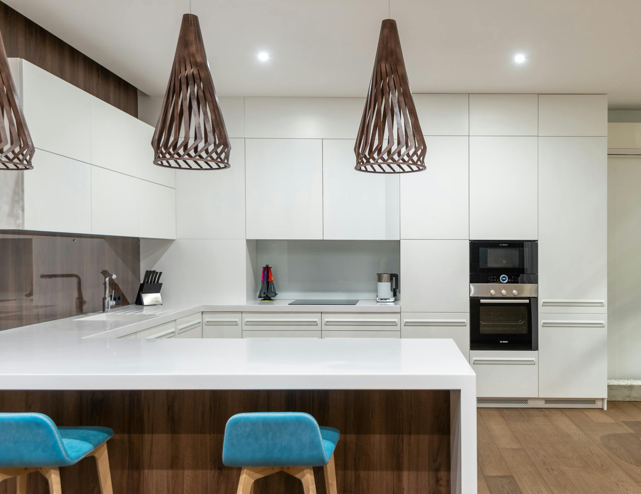 Turquoise chairs at counter with white cupboards and modern kitchenware in spacious light kitchen with hanging lamps in contemporary apartment remodel